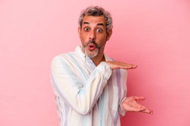 Orta yaşlı beyaz bir adam pembe arka planda izole edilmiş. Elleri arasında bir kopya alanı tutarken şok olmuş ve hayrete düşmüş..
