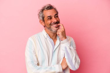 Orta yaşlı beyaz bir adam pembe arka planda izole edilmiş rahat bir şekilde fotokopi odasına bakan bir şey düşünüyor..