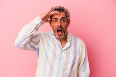 Pembe arka planda izole edilmiş orta yaşlı beyaz bir adam yüksek sesle bağırıyor, gözleri açık ve elleri gergin tutuyor..