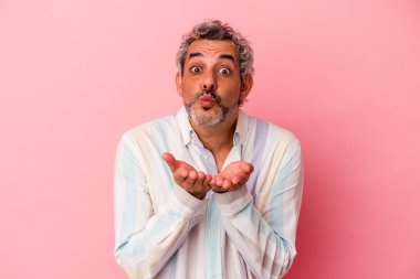 Orta yaşlı beyaz bir adam pembe arka planda izole edilmiş dudaklar kıvrılmış ve hava öpücüğü yollamak için avuç içi tutuyor..