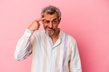 Pembe arka planda izole edilmiş orta yaşlı beyaz bir adam şakağı parmağıyla işaret ediyor, düşünüyor ve bir göreve odaklanıyor..