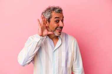 Orta yaşlı beyaz bir adam pembe arka planda izole edilmiş bir şekilde bir dedikoduyu dinlemeye çalışıyor..