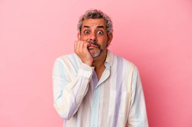 Orta yaşlı beyaz bir adam pembe arka planda izole edilmiş tırnak yiyor, gergin ve çok endişeli..