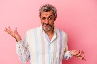 Orta yaşlı beyaz bir adam pembe arka planda izole edilmiş sorgulama jestinde şüphe ediyor ve omuz silkiyor..