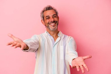 Pembe arka planda izole edilmiş orta yaşlı beyaz bir adam hoş bir yüz ifadesi sergiliyor..