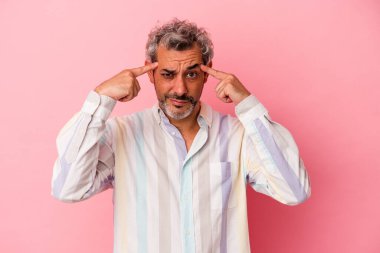 Pembe arka planda izole edilmiş orta yaşlı beyaz bir adam bir göreve odaklanmış, işaret parmaklarını işaret ediyor..