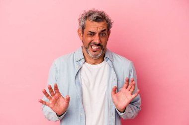 Orta yaşlı beyaz bir adam pembe arka planda izole edilmiş, tiksinti belirtisi gösteren birini reddediyor..