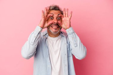 Pembe arka planda izole edilmiş orta yaşlı beyaz bir adam bir başarı fırsatı bulmak için gözlerini açık tutuyor..