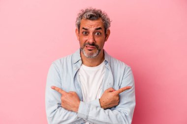 Orta yaşlı beyaz bir adam pembe arka plan noktalarında izole edilmiş, iki seçenek arasında seçim yapmaya çalışıyor..