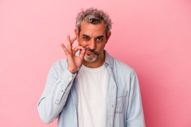 Orta yaşlı beyaz bir adam pembe arka planda izole edilmiş ve parmakları dudaklarında bir sır saklıyor..