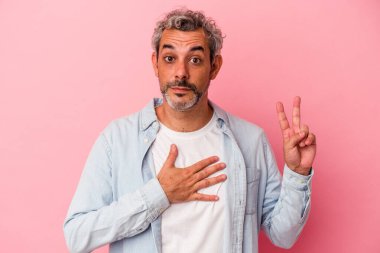 Orta yaşlı beyaz bir adam pembe arka planda izole edilmiş yemin ediyor, elini göğsüne koyuyor..