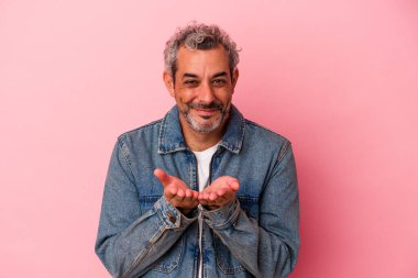 Orta yaşlı beyaz bir adam pembe arka planda izole edilmiş. Elinde avuç içi olan bir şeyle kameraya sunuyor..