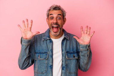 Orta yaşlı beyaz bir adam pembe arka planda izole edilmiş. Hoş bir sürpriz bekliyor. Heyecanlı ve el kaldırıyor..