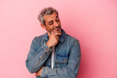 Pembe arka planda izole edilmiş orta yaşlı beyaz adam şüpheli ve şüpheci bir ifadeyle yana bakıyor..