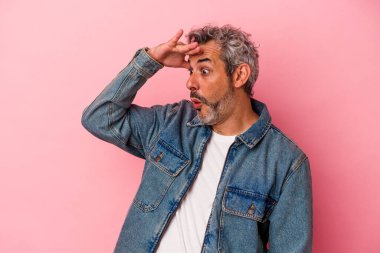 Orta yaşlı, beyaz bir adam pembe arka planda izole edilmiş. Uzağa bakıyor, elini alnına koyuyor..