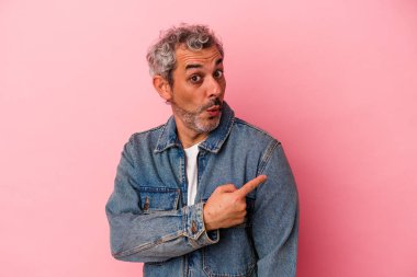 Orta yaşlı beyaz bir adam pembe arka planda izole edilmiş gülümsüyor ve boş alanda bir şeyler gösteriyor..