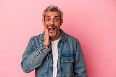 Pembe arka planda izole edilmiş orta yaşlı beyaz bir adam yüksek sesle bağırıyor, gözleri açık ve elleri gergin tutuyor..