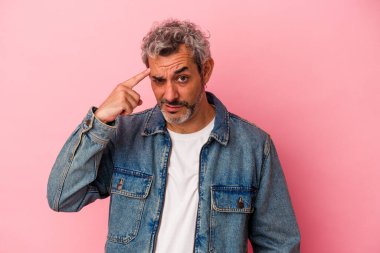 Pembe arka planda izole edilmiş orta yaşlı beyaz bir adam şakağı parmağıyla işaret ediyor, düşünüyor ve bir göreve odaklanıyor..