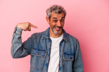Orta yaşlı beyaz bir adam pembe arka planda izole edilmiş. Elle bir gömlek fotokopi alanını işaret ediyor. Gururlu ve kendinden emin.