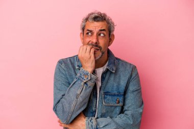 Orta yaşlı beyaz bir adam pembe arka planda izole edilmiş tırnak yiyor, gergin ve çok endişeli..