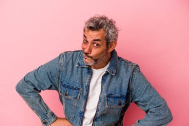 Pembe arka planda soyutlanmış orta yaşlı beyaz bir adam kafası karışmış, şüpheli ve kendinden emin değil..