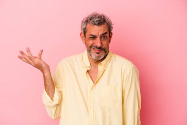 Orta yaşlı beyaz bir adam pembe arka planda izole edilmiş sorgulama jestinde şüphe ediyor ve omuz silkiyor..