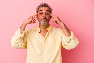 Pembe arka planda izole edilmiş orta yaşlı beyaz bir adam bir göreve odaklanmış, işaret parmaklarını işaret ediyor..