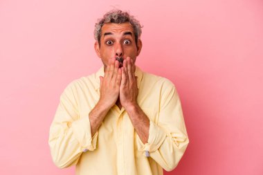 Pembe arka planda izole edilmiş orta yaşlı beyaz bir adam elleriyle ağzını kapatırken şok oldu..