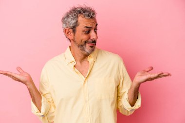 Orta yaşlı beyaz bir adam pembe arka planda izole edilmiş. Kafası karışmış ve omuz silkiyor..