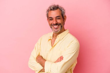 Pembe arka planda izole edilmiş orta yaşlı beyaz bir adam. Kendine güveniyor, kararlılıkla kollarını kavuşturuyor..