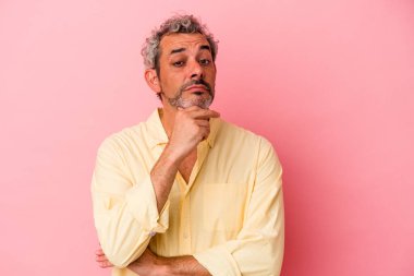 Orta yaşlı beyaz bir adam pembe arka planda izole edilmiş şüpheli, belirsiz, seni muayene ediyor..