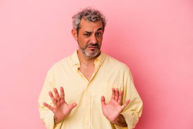Orta yaşlı beyaz bir adam pembe arka planda izole edilmiş, tiksinti belirtisi gösteren birini reddediyor..