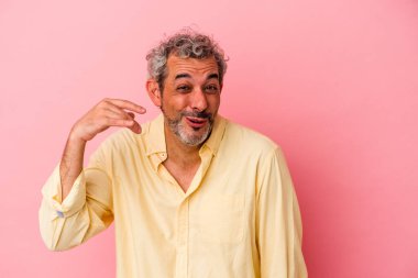 Orta yaşlı beyaz bir adam pembe arka planda izole edilmiş bir şekilde bir şeye gülüyor, ağızlarını ellerle kapatıyor..