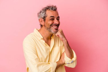Orta yaşlı beyaz adam pembe arka planda izole edilmiş mutlu ve kendinden emin gülümsüyor, çenesine elleriyle dokunuyor..