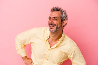 Pembe arka planda izole edilmiş orta yaşlı beyaz bir adam mutlu bir şekilde gülüyor ve ellerini karnının üstünde tutarak eğleniyor..
