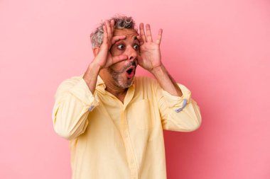 Pembe arka planda izole edilmiş orta yaşlı beyaz bir adam bir başarı fırsatı bulmak için gözlerini açık tutuyor..