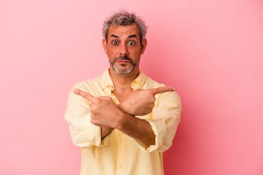 Orta yaşlı beyaz bir adam pembe arka plan noktalarında izole edilmiş, iki seçenek arasında seçim yapmaya çalışıyor..