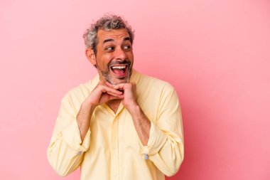 Pembe arka planda izole edilmiş orta yaşlı beyaz bir adam ellerini çenesinin altında tutuyor, mutlu bir şekilde yana bakıyor..