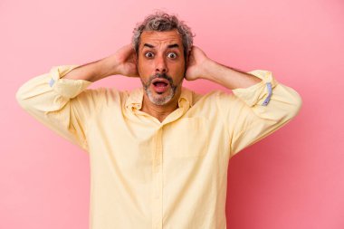 Orta yaşlı, beyaz bir adam pembe arka planda izole edilmiş kulakları kulaklarıyla kapatıyor ve çok fazla ses duymamaya çalışıyor..