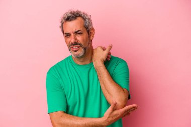 Orta yaşlı beyaz bir adam pembe arka planda izole edilmiş dirsek masajı yapıyor, kötü bir hareketin ardından acı çekiyor..