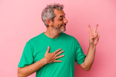 Orta yaşlı beyaz bir adam pembe arka planda izole edilmiş yemin ediyor, elini göğsüne koyuyor..