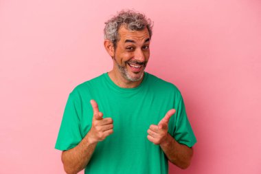 Pembe arka planda izole edilmiş orta yaşlı beyaz bir adam parmaklarıyla ön tarafı işaret ediyor..