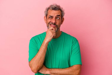 Pembe arka planda izole edilmiş orta yaşlı beyaz adam şüpheli ve şüpheci bir ifadeyle yana bakıyor..