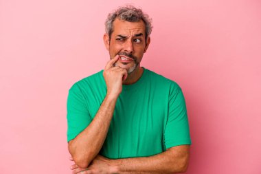Pembe arka planda izole edilmiş orta yaşlı beyaz adam şüpheli ve şüpheci bir ifadeyle yana bakıyor..