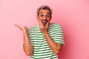 Pembe arka planda izole edilmiş orta yaşlı beyaz bir adam bir avuç içinde fotokopi alanı tutuyor, el üstünde tutuyor. Şaşırmış ve mutlu..