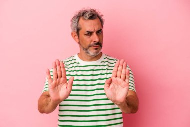 Orta yaşlı, beyaz bir adam pembe arka planda izole edilmiş, elini uzatmış, dur işareti göstererek seni engelliyor..