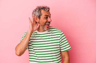 Orta yaşlı beyaz bir adam pembe arka planda izole edilmiş bir şekilde bir dedikoduyu dinlemeye çalışıyor..