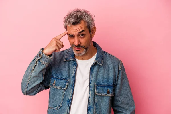 Pembe arka planda izole edilmiş orta yaşlı beyaz bir adam şakağı parmağıyla işaret ediyor, düşünüyor ve bir göreve odaklanıyor..