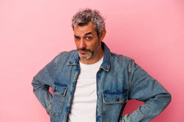 Orta yaşlı beyaz bir adam pembe arka planda izole edilmiş hoşnutsuzca kaşlarını çatmış, kollarını kavuşturmuş..