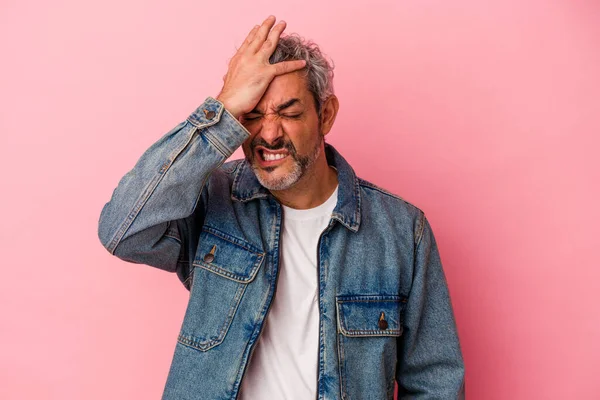 Orta yaşlı beyaz bir adam pembe arka planda izole edilmiş bir şekilde bir şeyi unutuyor. Alnına avuç içi ve kapalı gözlerle vuruyor..
